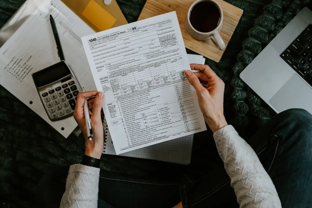 Hands holding a tax form next to a calculator and laptop