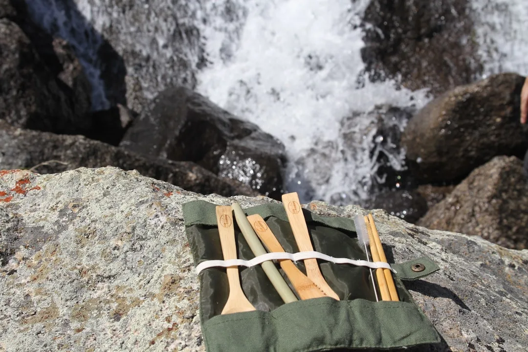 Bambus-Zahnbürsten im Leinenstoff-Etui auf Felsen neben einem Wasserfall – Zero-Waste-Reiseutensilien