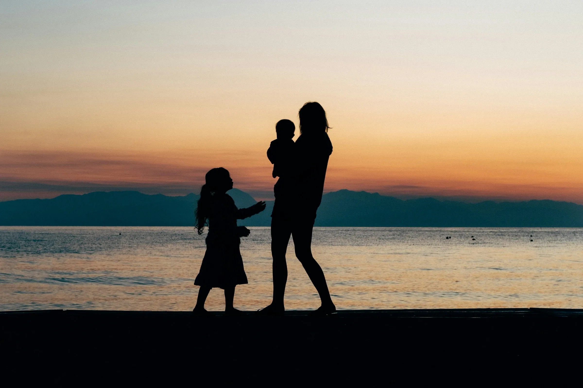 Mutter mit zwei Kindern beim Spaziergang am Sandstrand bei Sonnenaufgang auf Korfu, Griechenland