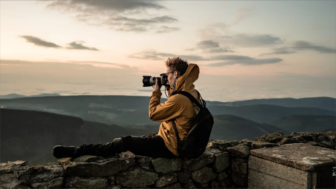 Outdoor photographer with camera on stone wall, photographing mountain landscape at dusk