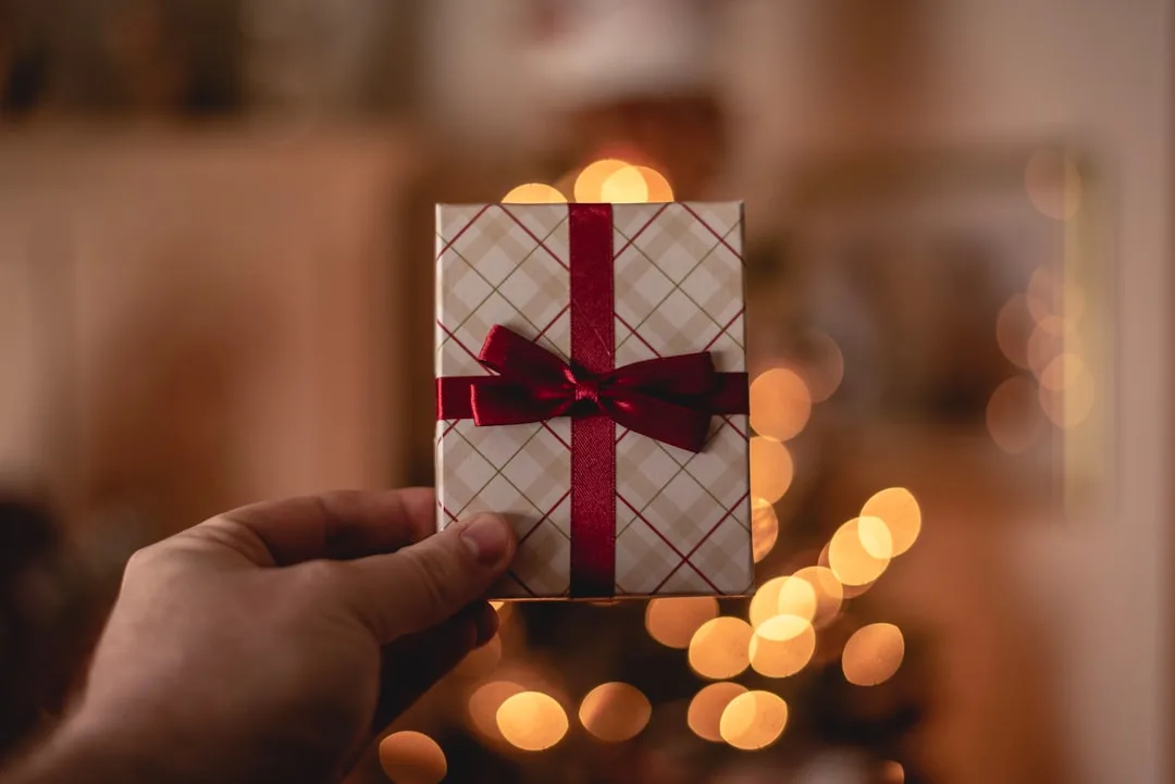Hand holding a small gift with red ribbon against warm bokeh background — travel gift voucher