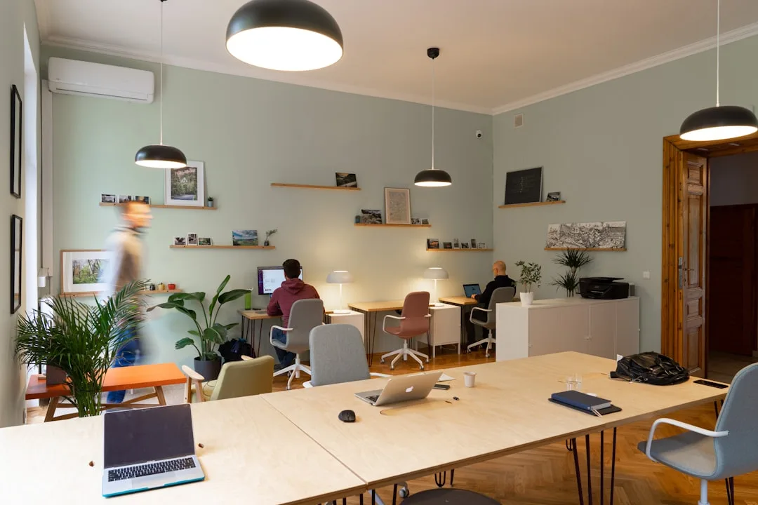 Bright open coworking space with long wooden tables, pendant lights and people working on laptops