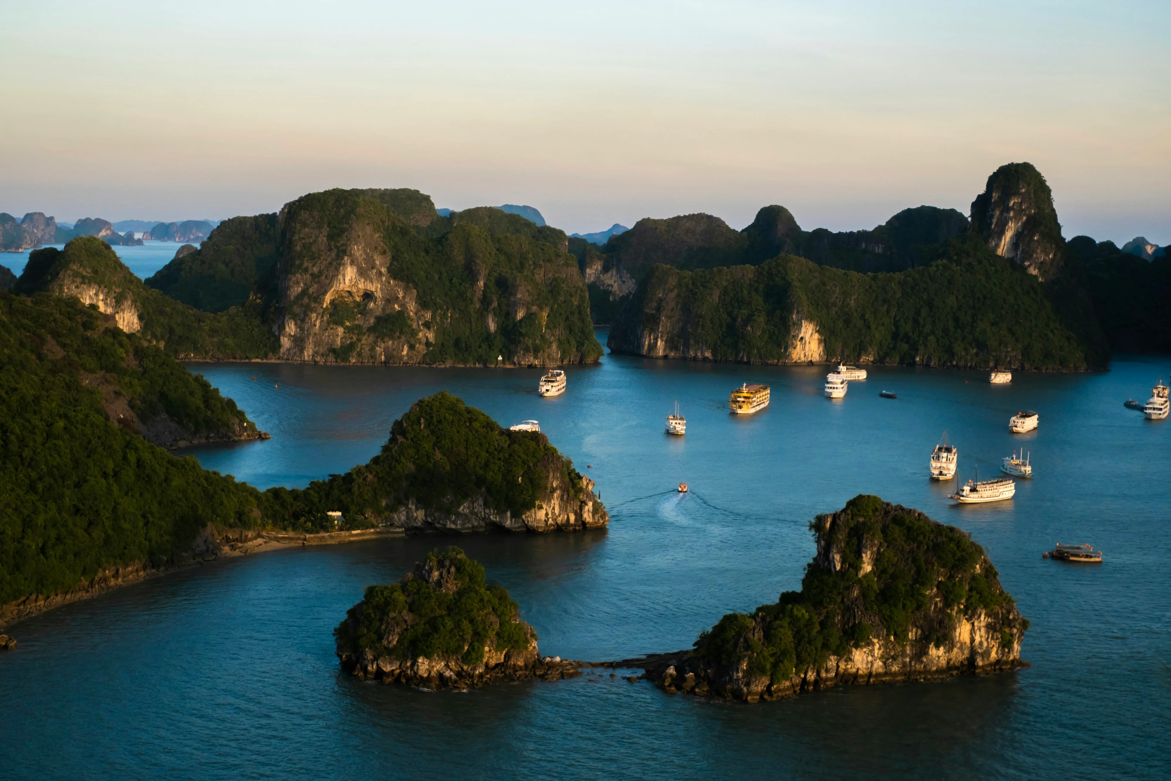 Halong-Bucht mit Kalkstein-Inseln und Ausflugsschiffen bei Dämmerung, Vietnam
