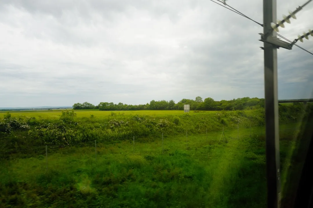 Wide green countryside landscape with gentle hills and overcast sky — slow travel and deceleration